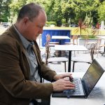 Phil Creighton at an open air cafe typing a review on a laptop