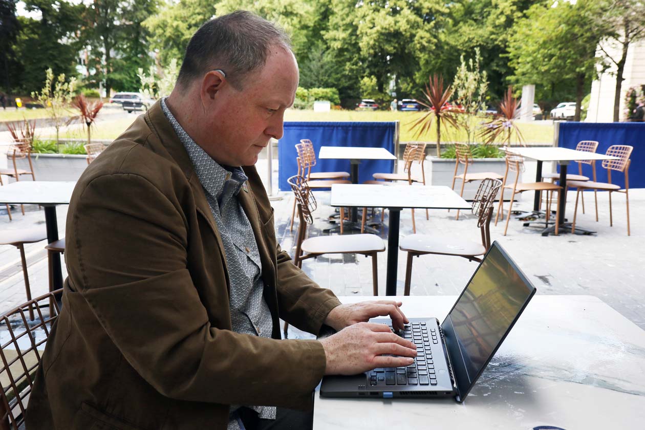 Phil Creighton at an open air cafe typing a review on a laptop