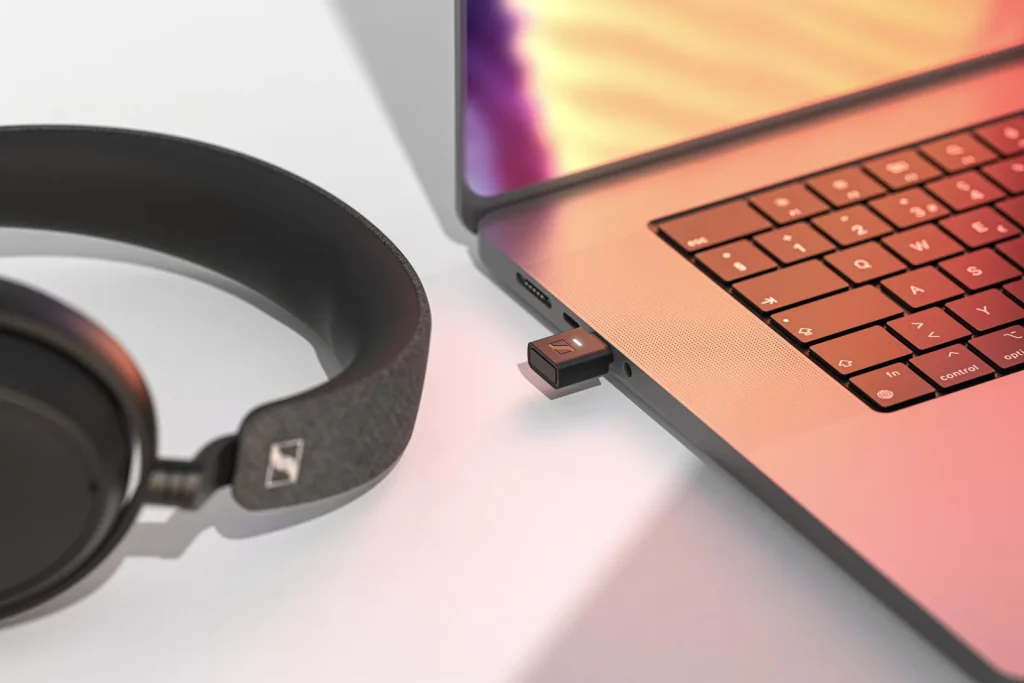 The Sennheiser BTD 700 plugged into a laptop with a pair of headphones next to it 