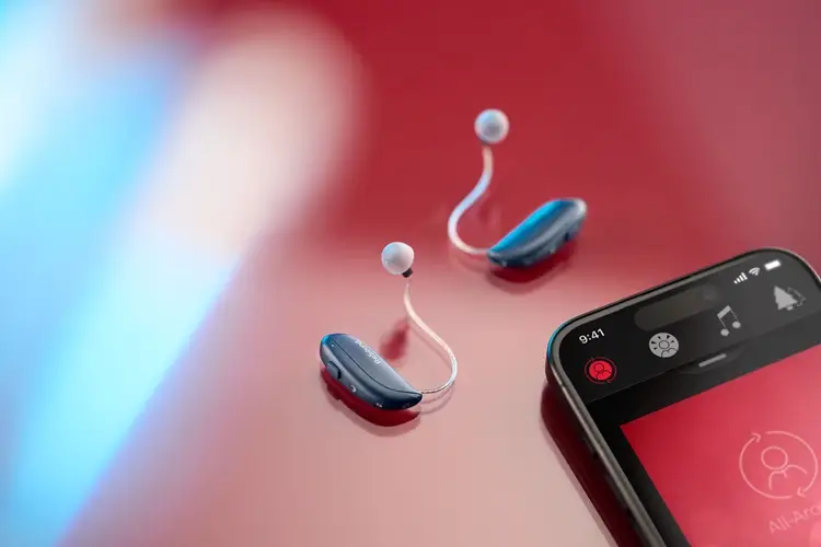 The ReSound Vivia hearing aids on a red background. On the right hand side of the image is a mobile phone showing the ReSound app