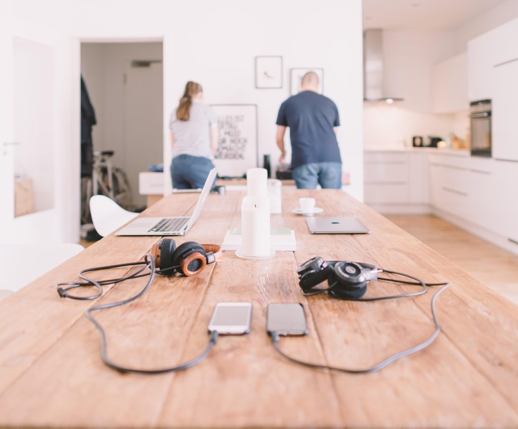 Some headphones on a table. They are plugged into mobile phones. Next to them are laptops and candles. 
