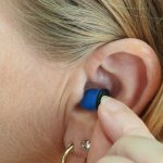 A person inserting a hearing aid into their ear. We do not know if they have Auracast in the ear. the RNID wants to see Auracast adopted by hearing aid manufacturers
