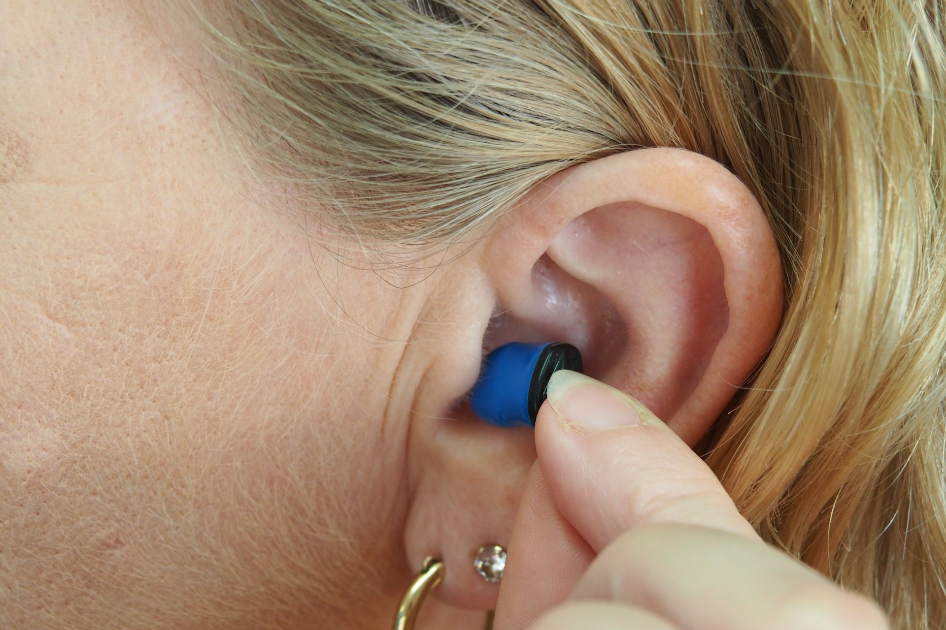 A person inserting a hearing aid into their ear. We do not know if they have Auracast in the ear. the RNID wants to see Auracast adopted by hearing aid manufacturers