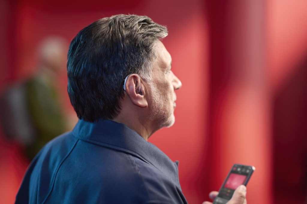 A person wearing the ReSound Enzo IA hearing aid while holding the phone app in their hands