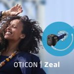 Oticon launch picture for Oticon Zeal featuring a happy woman dancing with her hand in the air. In a blue swoosh is a picture of the Oticon Zeal which comes with Google Fast Pair