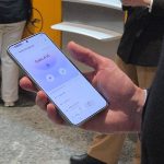 A person holding a mobile phone at Frankfurt Airport showing they are tuned into the Auracast at Gate A16