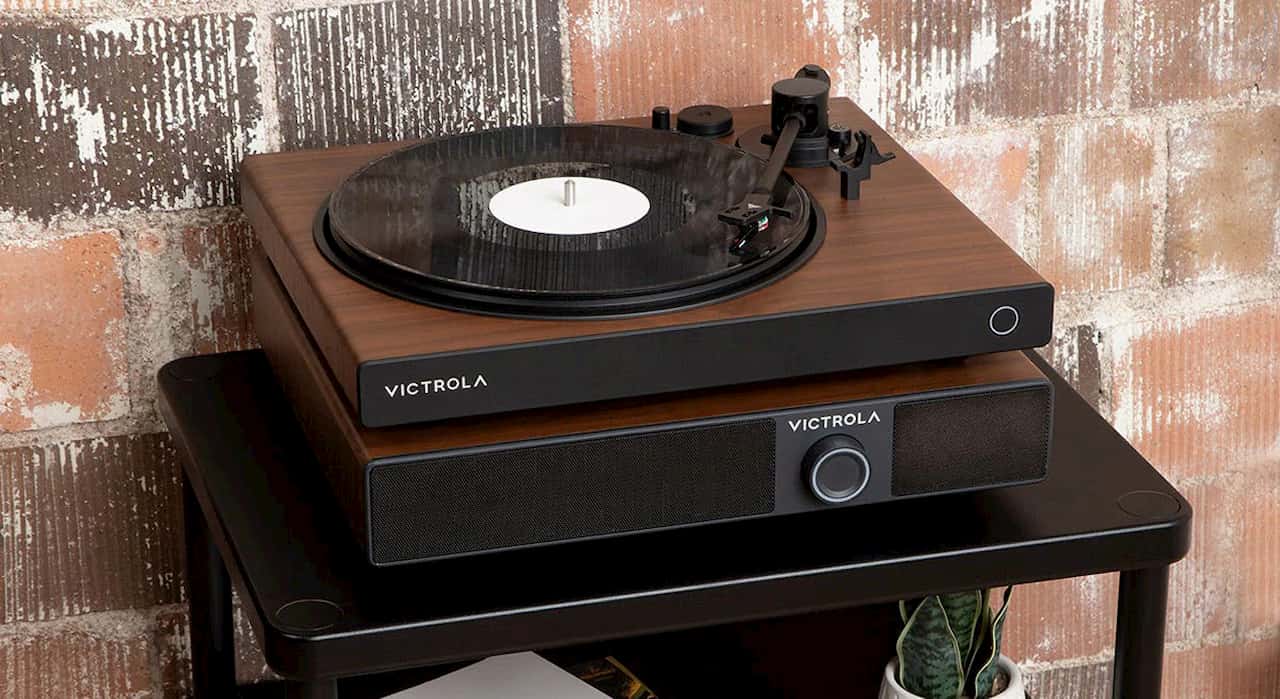 Victrola Soundstage sitting on top of a table. It is a speaker system with a turntable on top of it. Behind it is a brick wall