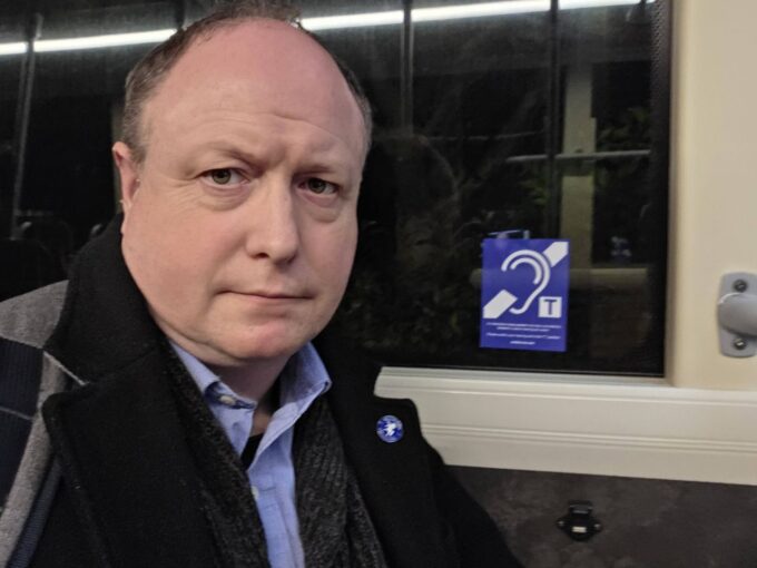 Phil Creighton on a bus with a Telecoil logo behind him