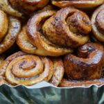 A tray of freshly baked, glazed cinnamon buns, referencing the "Cinnamon Bun" codename for Android 17, which introduces key improvements to Auracast and hearing aid compatibility Beth macdonald V6LEV6CBVLw unsplash