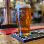 A close-up, shallow depth-of-field photo of a pint of amber ale in a Timothy Taylor glass sitting on a bar mat in a pub