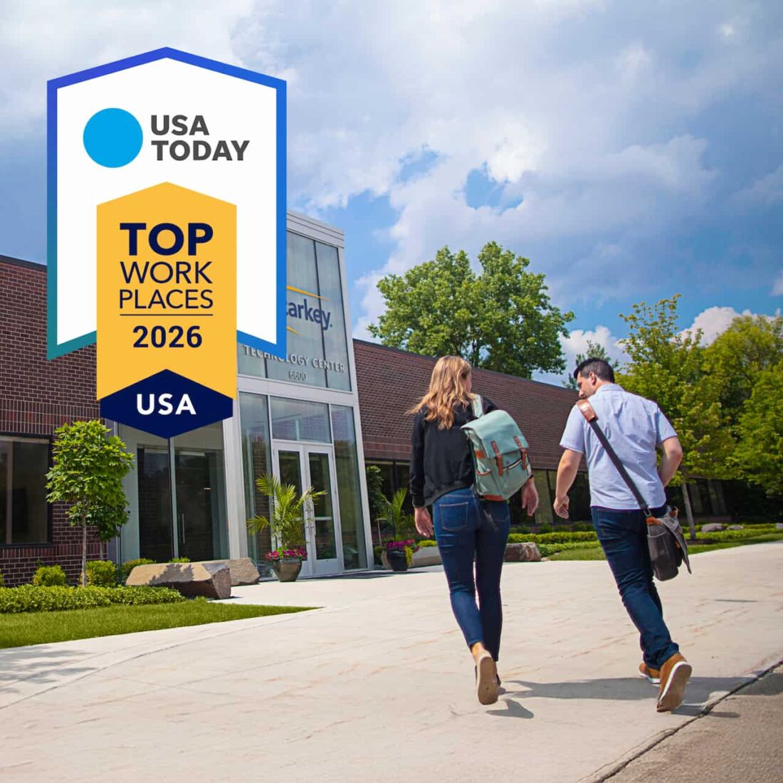 Starkey is celebrating its USA Today Top Workplaces award. The image shows the award logo and two people walking towards the entrance of Starkey HQ. They have their backs to us and we can see one has a rucksack, the other a satchel. It's a bright sunny day with blue sky and happy clouds