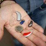 An outstretched hand holding three different hearing aids and a Euro coin to show the size