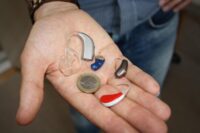 An outstretched hand holding three different hearing aids and a Euro coin to show the size