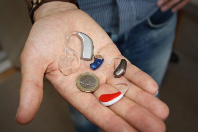 An outstretched hand holding three different hearing aids and a Euro coin to show the size