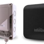 Two Williams AV hardware updates are shown side by side against a white background in Infinium update.jpg. On the left, a cutaway view shows an Infinium transmitter positioned inside a rugged, protective outdoor enclosure with a cable entry point at the bottom. On the right, a standalone square Infinium transmitter is presented in a matte black finish with a small blue status light glowing next to the logo.