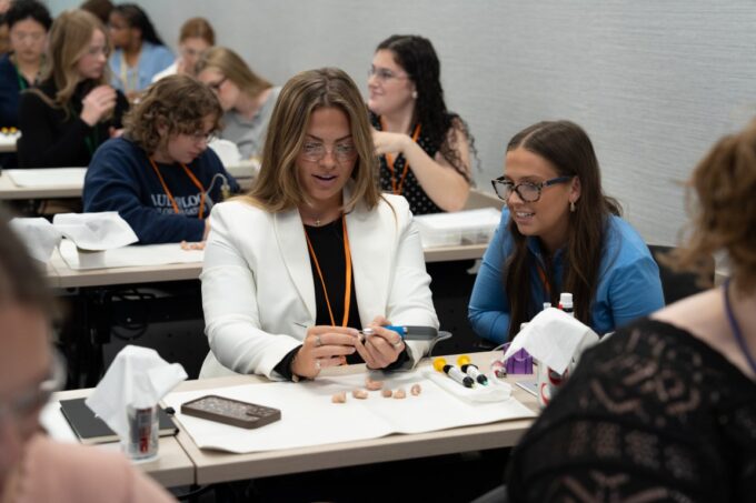 Two audiology students at a classroom desk examining and working on hearing aid components during a workshop