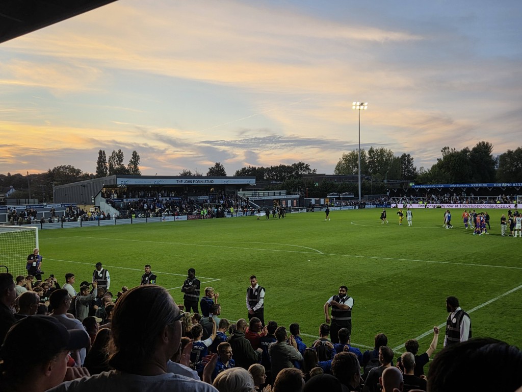 The sun sets while fans watch a game of football in a stadium