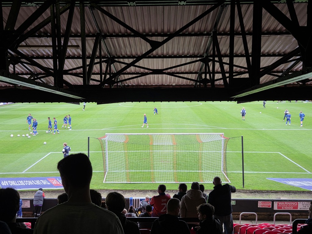 An old-school football terrace with a restricted view of the pitch. The goal can be seen.