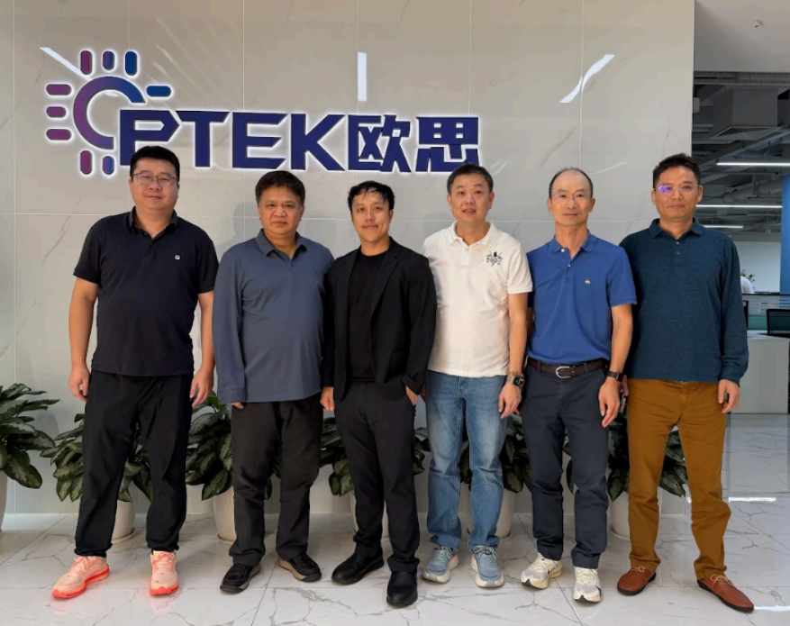 Senior leadership representatives from Optek, Audeara, and Eastech standing together in front of the Optek company logo on an office wall