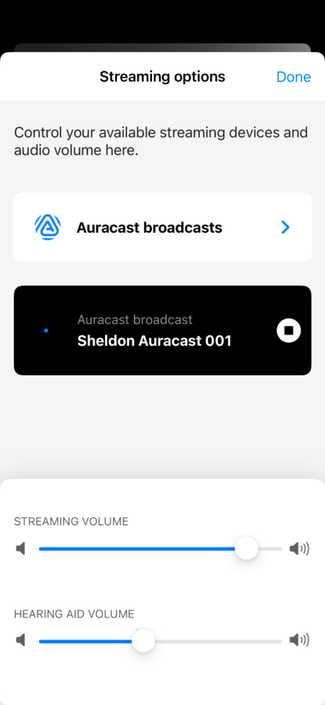 A screenshot of a dark-themed mobile app titled 'Streaming audio', with icons for sound adjustment, programs, and hearing health. It features volume sliders for 'Streaming Volume' and 'Hearing Aid Mic', and shows an active connection to 'Sheldon Auracast 001'