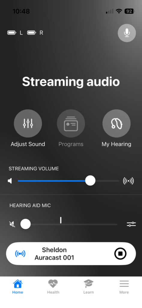 A screenshot of a mobile phone app showing 'Streaming options' for Auracast broadcasts, including an entry for 'Sheldon Auracast 001', and independent volume sliders for 'Streaming Volume' and 'Hearing Aid Volume'