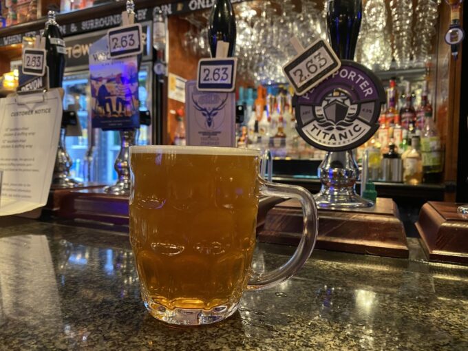 Dimpled glass handle tankard of golden ale resting on a dark polished bar counter in front of traditional real ale handpumps