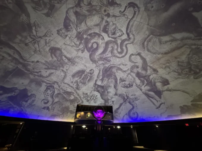 Detailed celestial map and mythological constellations projected across the dome of the James S. McDonnell Planetarium, with the illuminated star projector in the centre foreground