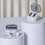 White Samsung Galaxy Buds4 series earbuds displayed on white cylindrical pedestals, with one pair inside an open charging case and another resting beside a closed case