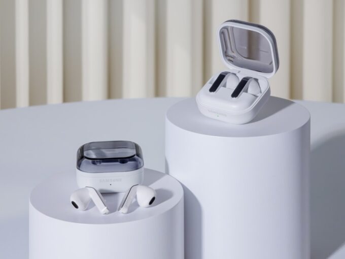 White Samsung Galaxy Buds4 series earbuds displayed on white cylindrical pedestals, with one pair inside an open charging case and another resting beside a closed case
