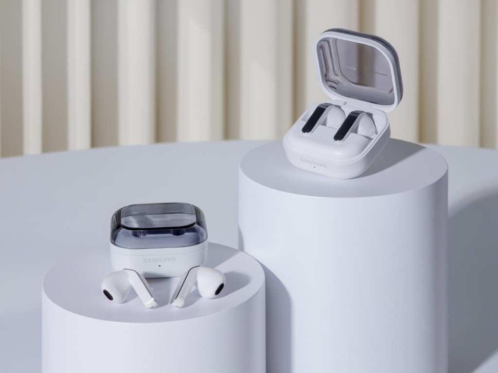 White Samsung Galaxy Buds4 series earbuds displayed on white cylindrical pedestals, with one pair inside an open charging case and another resting beside a closed case